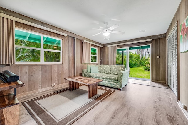 living room featuring ceiling fan, wooden walls, and light wood-type flooring