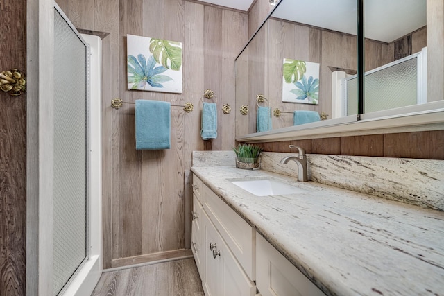 bathroom with hardwood / wood-style floors, vanity, a shower with door, and wooden walls