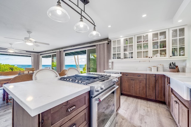 kitchen with a center island, white cabinets, hanging light fixtures, stainless steel stove, and light hardwood / wood-style flooring