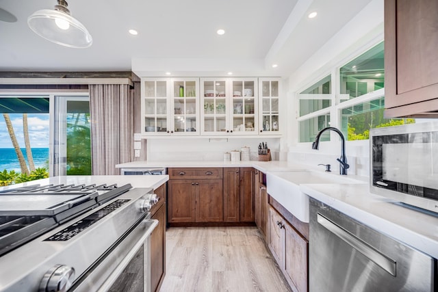 kitchen featuring appliances with stainless steel finishes, sink, pendant lighting, a water view, and light hardwood / wood-style flooring