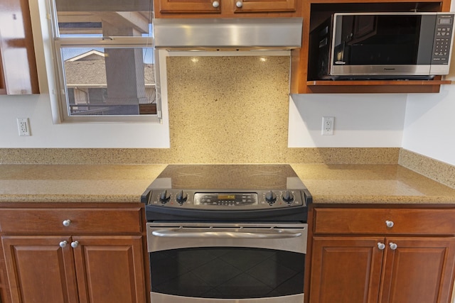 kitchen featuring light stone counters, exhaust hood, and appliances with stainless steel finishes