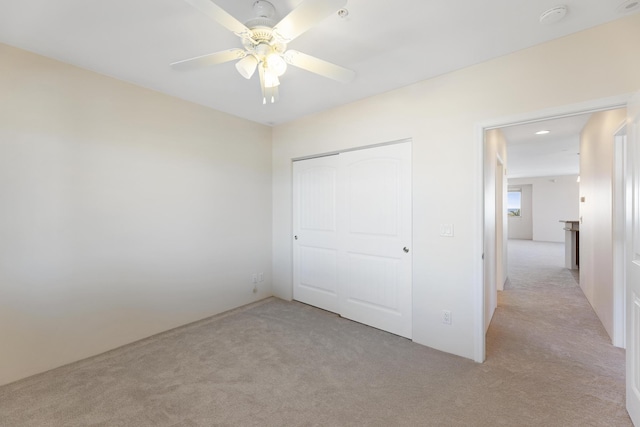 unfurnished bedroom featuring light carpet, ceiling fan, and a closet