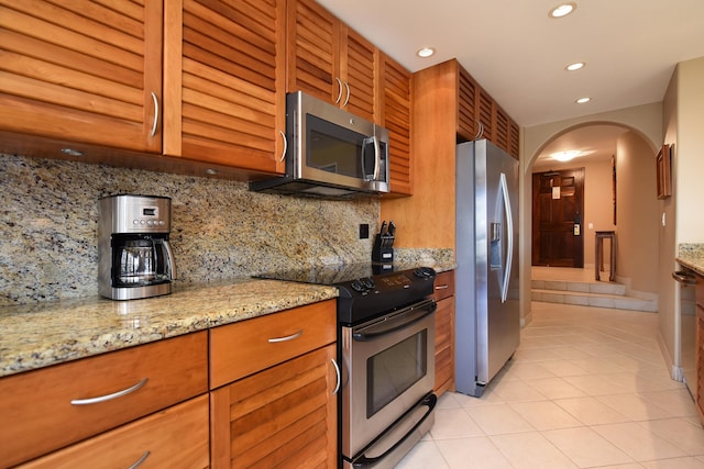 kitchen with light stone counters, light tile patterned floors, stainless steel appliances, and tasteful backsplash