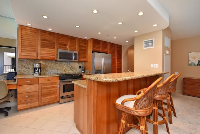 kitchen featuring a kitchen bar, decorative backsplash, kitchen peninsula, stainless steel appliances, and light tile patterned flooring