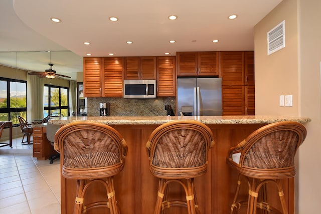 kitchen with kitchen peninsula, appliances with stainless steel finishes, tasteful backsplash, and light tile patterned flooring