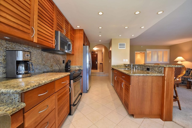 kitchen featuring appliances with stainless steel finishes, a kitchen breakfast bar, sink, kitchen peninsula, and light stone counters