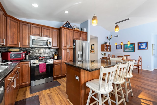 kitchen featuring stainless steel appliances, lofted ceiling, tasteful backsplash, light wood-style floors, and a kitchen breakfast bar