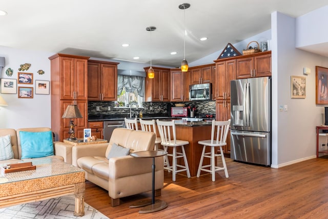 kitchen with stainless steel appliances, dark countertops, backsplash, a kitchen island, and wood finished floors