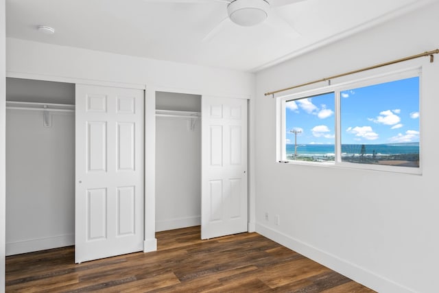 unfurnished bedroom featuring two closets, ceiling fan, and dark hardwood / wood-style floors