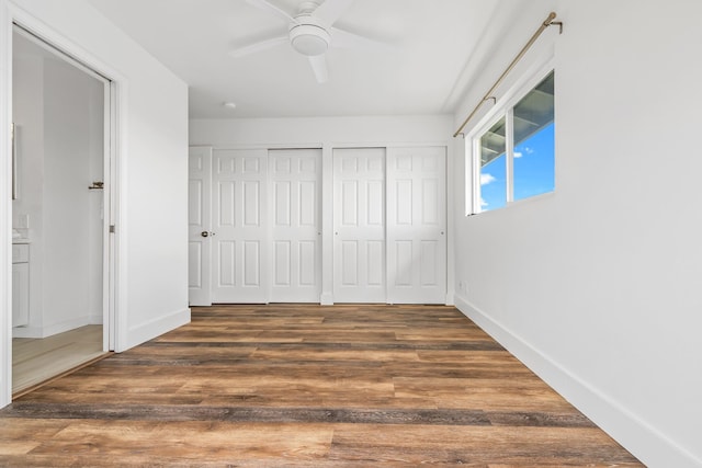 unfurnished bedroom with dark wood-type flooring, ceiling fan, and multiple closets