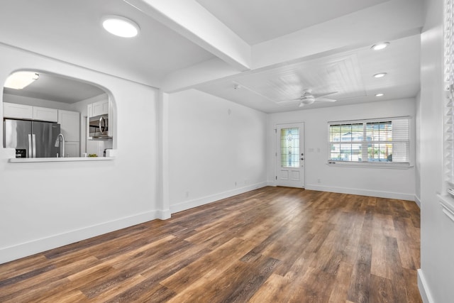 unfurnished living room featuring ceiling fan, dark hardwood / wood-style floors, and beamed ceiling