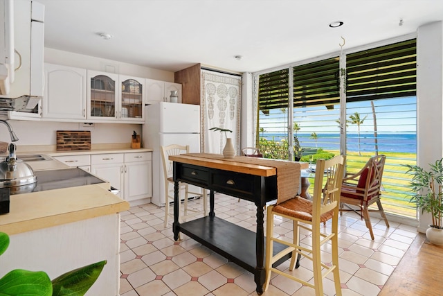 kitchen featuring a sink, white cabinetry, freestanding refrigerator, glass insert cabinets, and light floors