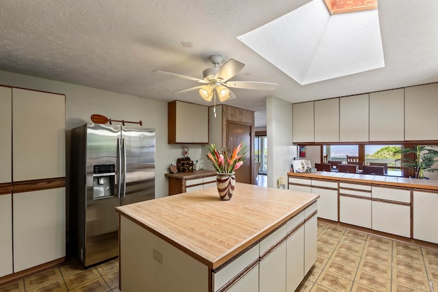 kitchen with stainless steel fridge, white cabinets, a center island, and a skylight