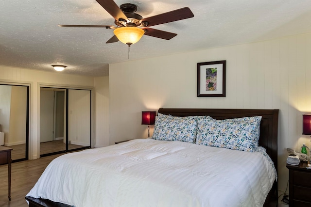 bedroom featuring ceiling fan, hardwood / wood-style flooring, multiple closets, and a textured ceiling