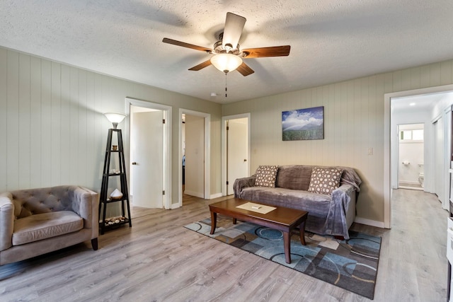 living room with ceiling fan, a textured ceiling, light wood-type flooring, and wood walls