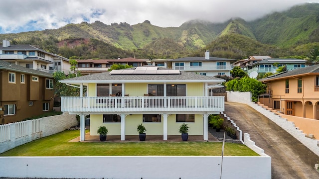 rear view of house with a balcony, a mountain view, and a lawn