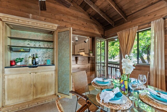 dining space with carpet floors, lofted ceiling with beams, wood ceiling, and wood walls