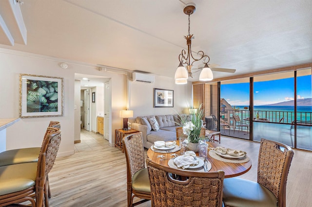 dining area with a chandelier, light wood-type flooring, floor to ceiling windows, a water view, and a wall mounted air conditioner