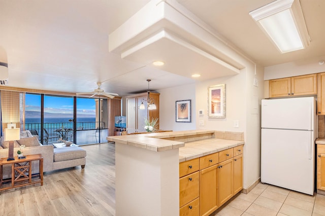 kitchen featuring tile counters, light brown cabinets, white fridge, kitchen peninsula, and expansive windows