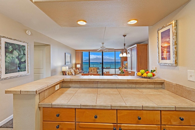 kitchen with ceiling fan, kitchen peninsula, a textured ceiling, a water view, and tile counters