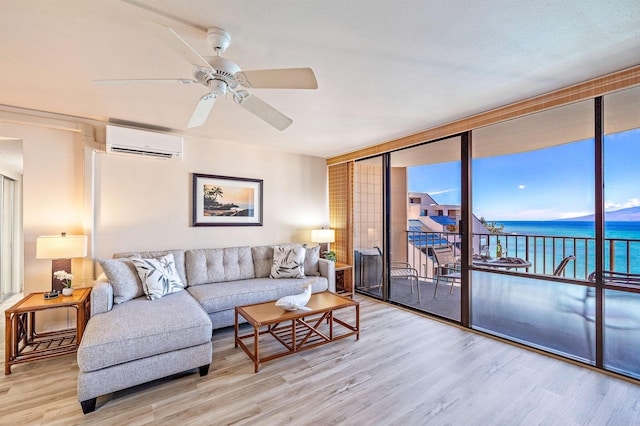 living room with ceiling fan, an AC wall unit, expansive windows, light wood-type flooring, and a water view