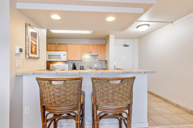 kitchen with light brown cabinetry, a kitchen breakfast bar, white appliances, and kitchen peninsula