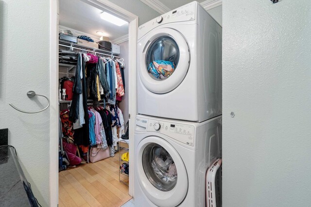 clothes washing area featuring crown molding, wood-type flooring, and stacked washer and dryer