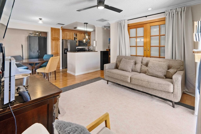 living room featuring ceiling fan, crown molding, light hardwood / wood-style floors, and a textured ceiling