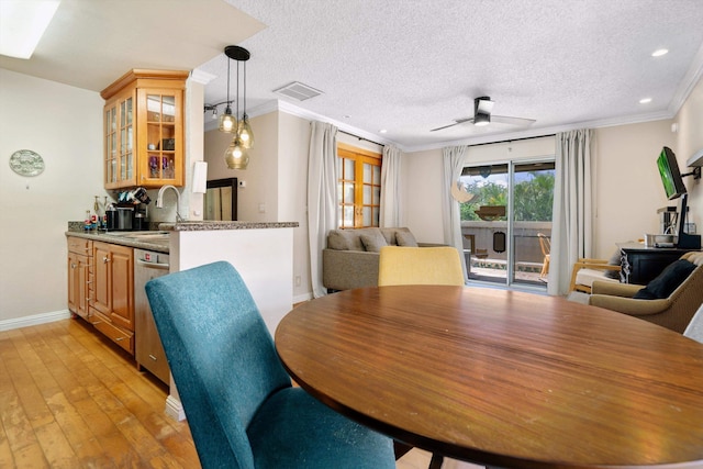 dining room with crown molding, ceiling fan, a textured ceiling, wet bar, and light hardwood / wood-style floors