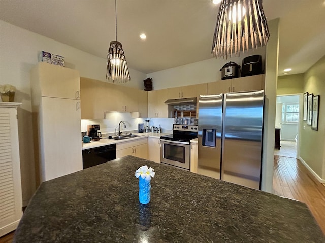 kitchen featuring under cabinet range hood, dark stone counters, appliances with stainless steel finishes, wood finished floors, and a sink