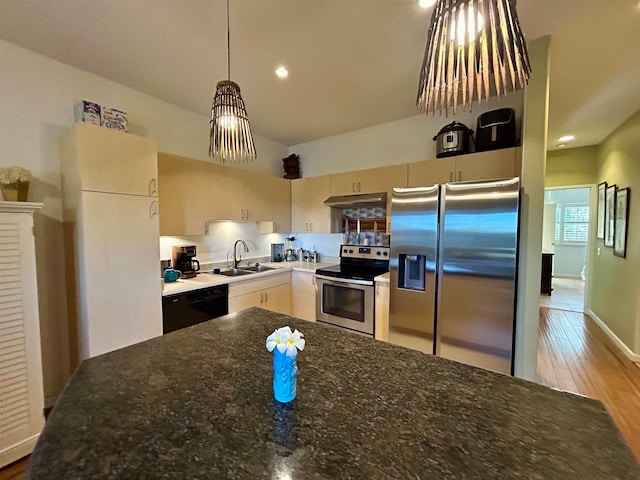 kitchen featuring hanging light fixtures, light hardwood / wood-style floors, dark stone countertops, stainless steel appliances, and sink