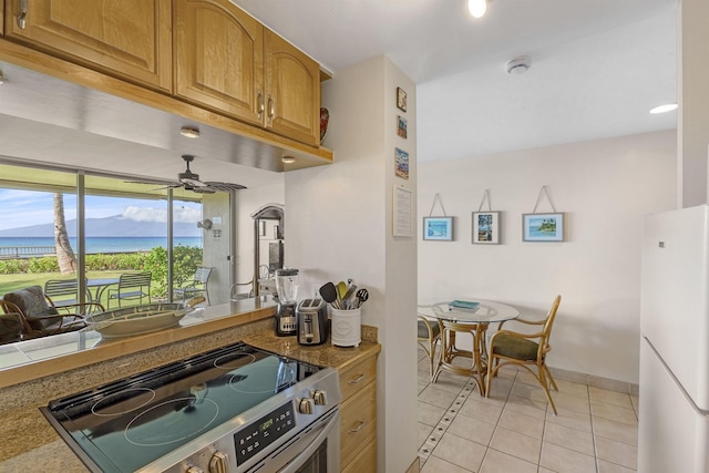 kitchen featuring electric stove, brown cabinets, light tile patterned floors, freestanding refrigerator, and ceiling fan