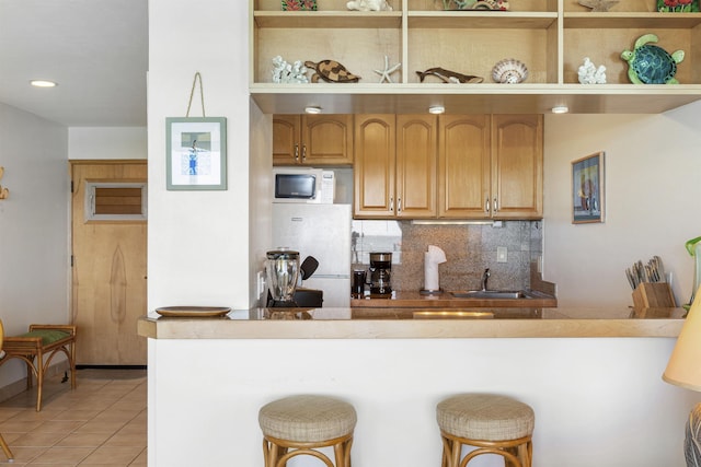 kitchen with light tile patterned floors, decorative backsplash, a sink, and a kitchen breakfast bar