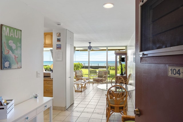 doorway featuring ceiling fan, a wall of windows, light tile patterned flooring, and a water view