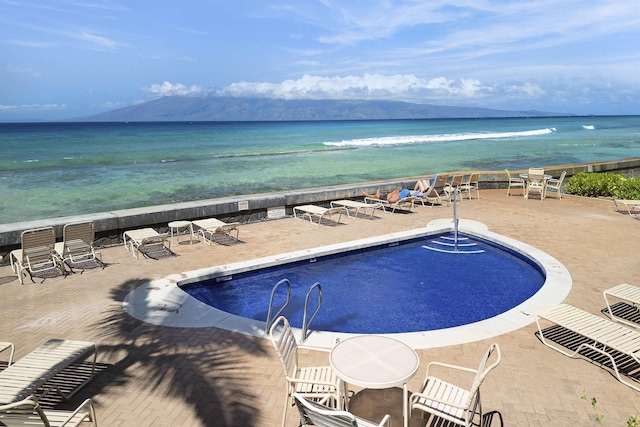 community pool with a patio area, a water view, and a beach view