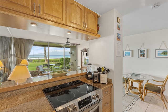 kitchen featuring brown cabinets, a ceiling fan, stainless steel range with electric cooktop, and light tile patterned floors