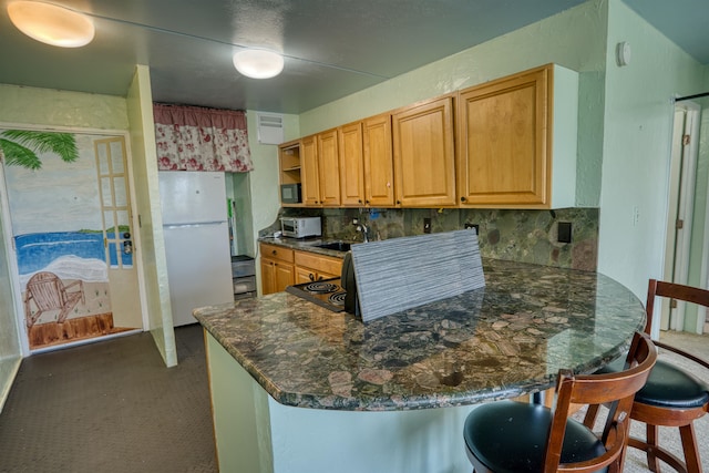 kitchen with white refrigerator, kitchen peninsula, backsplash, and a breakfast bar