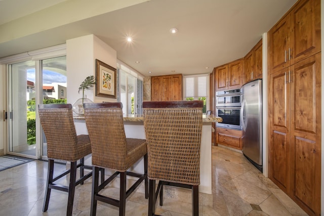 kitchen featuring recessed lighting, stainless steel appliances, a breakfast bar, a peninsula, and brown cabinetry