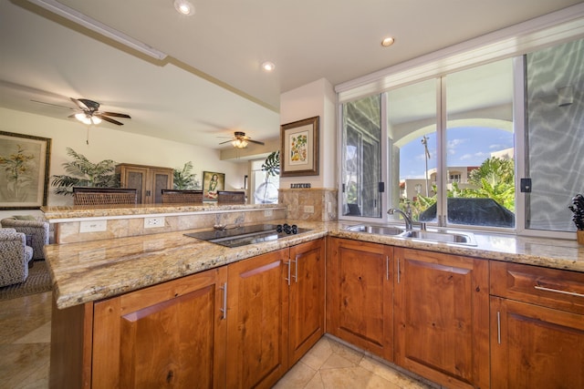 kitchen with light stone counters, black electric stovetop, open floor plan, a sink, and a peninsula