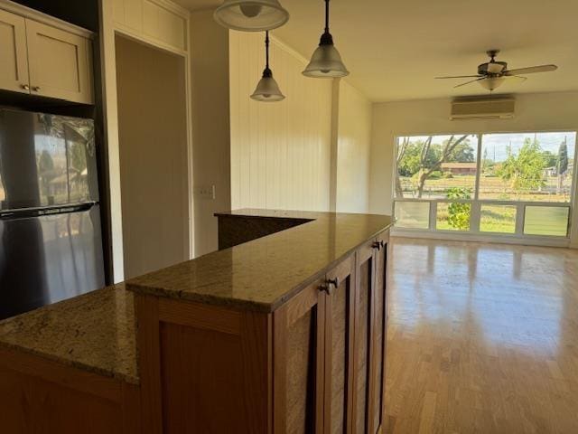 kitchen featuring stone counters, fridge, hanging light fixtures, ceiling fan, and a wall mounted AC