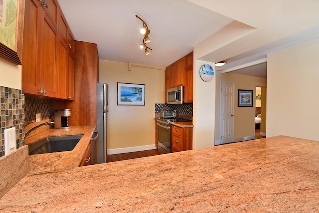 kitchen with backsplash, light stone counters, stainless steel appliances, sink, and wood-type flooring