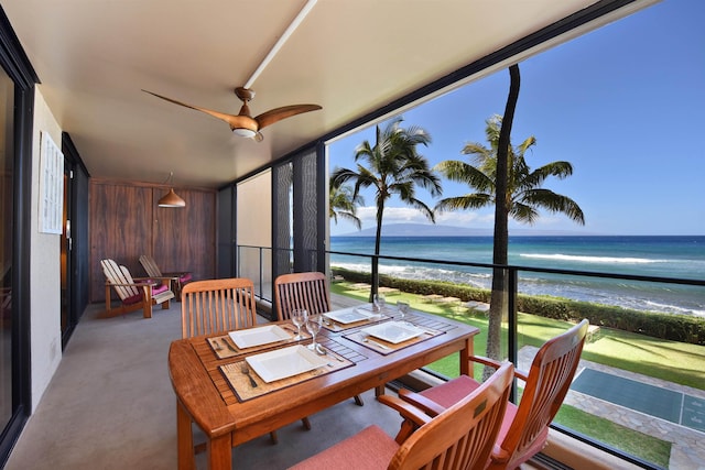 sunroom / solarium featuring ceiling fan, a water view, and a beach view