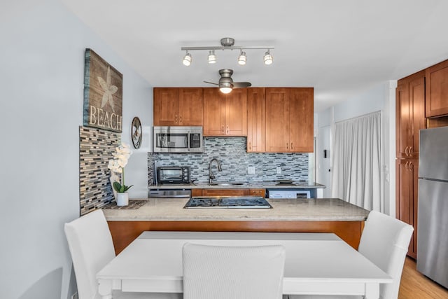 kitchen with a ceiling fan, a sink, a peninsula, decorative backsplash, and stainless steel appliances
