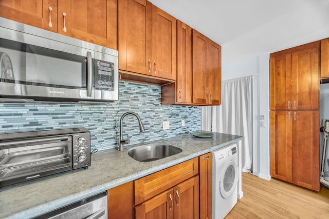 kitchen featuring stainless steel microwave, a sink, washer / dryer, light wood-style flooring, and backsplash