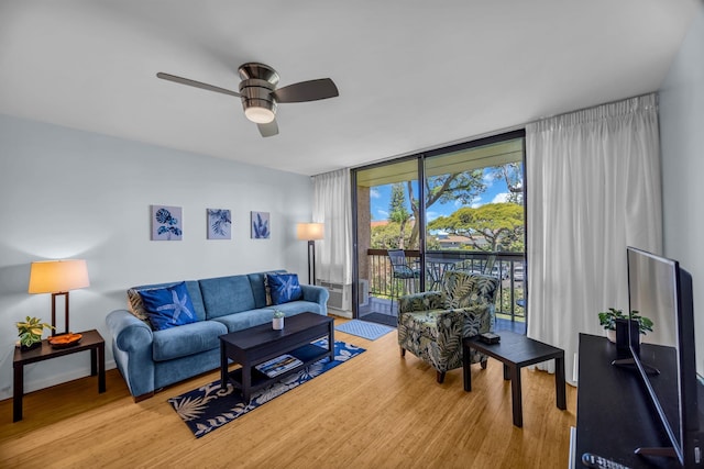 living area with a ceiling fan, a wall of windows, and wood finished floors