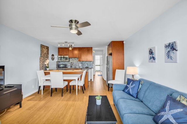 living area featuring rail lighting, light wood-style flooring, baseboards, and a ceiling fan