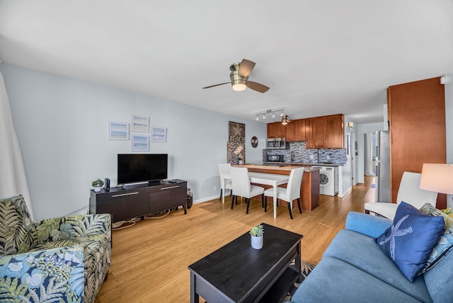 living area featuring a ceiling fan, light wood-style flooring, baseboards, track lighting, and washer / dryer
