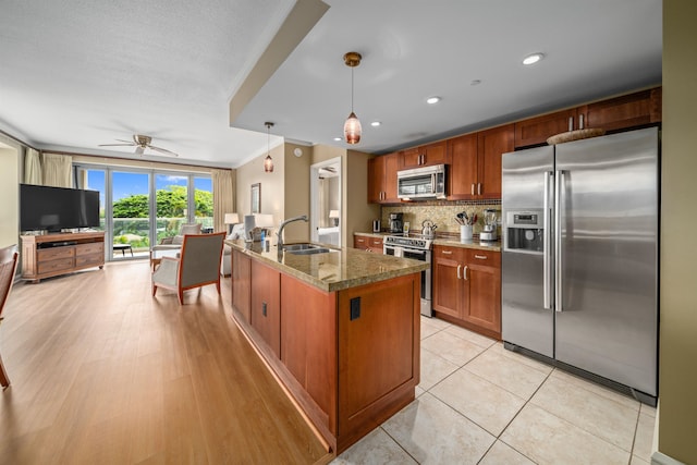 kitchen featuring backsplash, a center island with sink, sink, decorative light fixtures, and stainless steel appliances