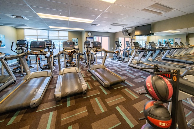 gym featuring dark colored carpet, plenty of natural light, and a drop ceiling