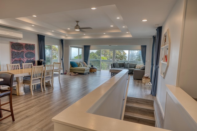 interior space with hardwood / wood-style floors, a tray ceiling, an AC wall unit, and ceiling fan